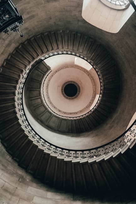 An indoor staircase with wooden handrails and black metal balusters ascending from a ground floor to an upper level in a residential property. The staircase is partially covered with a red patterned c